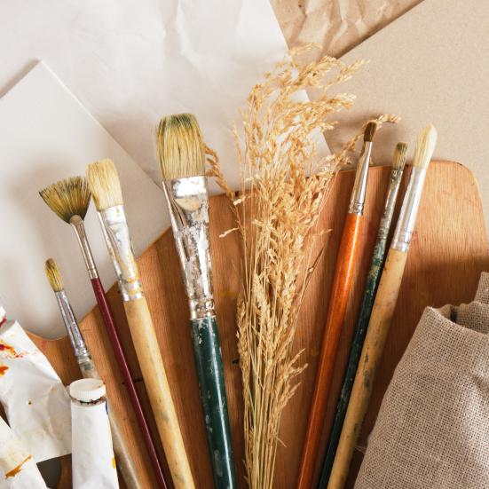 Papirmaterialer med pensler og tuber med maling liggende ovenpå.