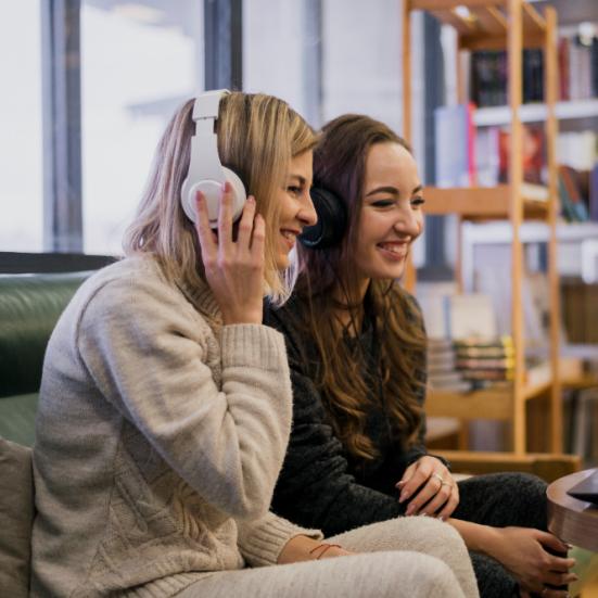 To kvinder, der sidder og taler foran en laptop. Den ene har høretelefoner på.