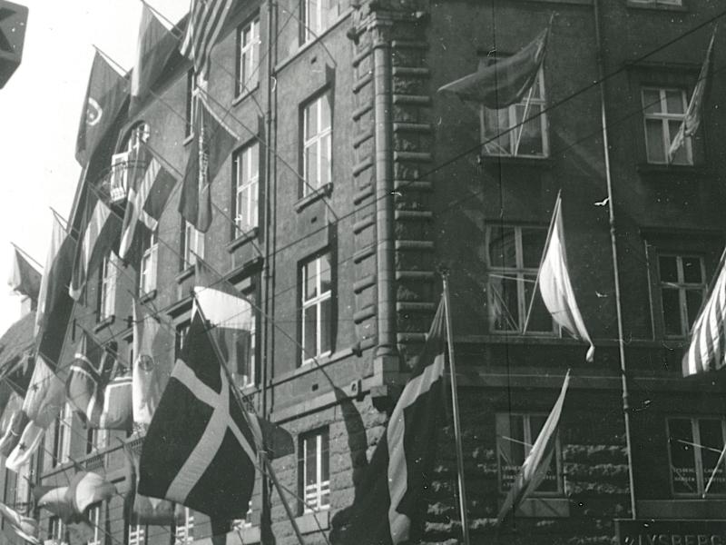 Foto i sort/hvid af et lejlighedskompleks med flag hængende ud af vinduerne.